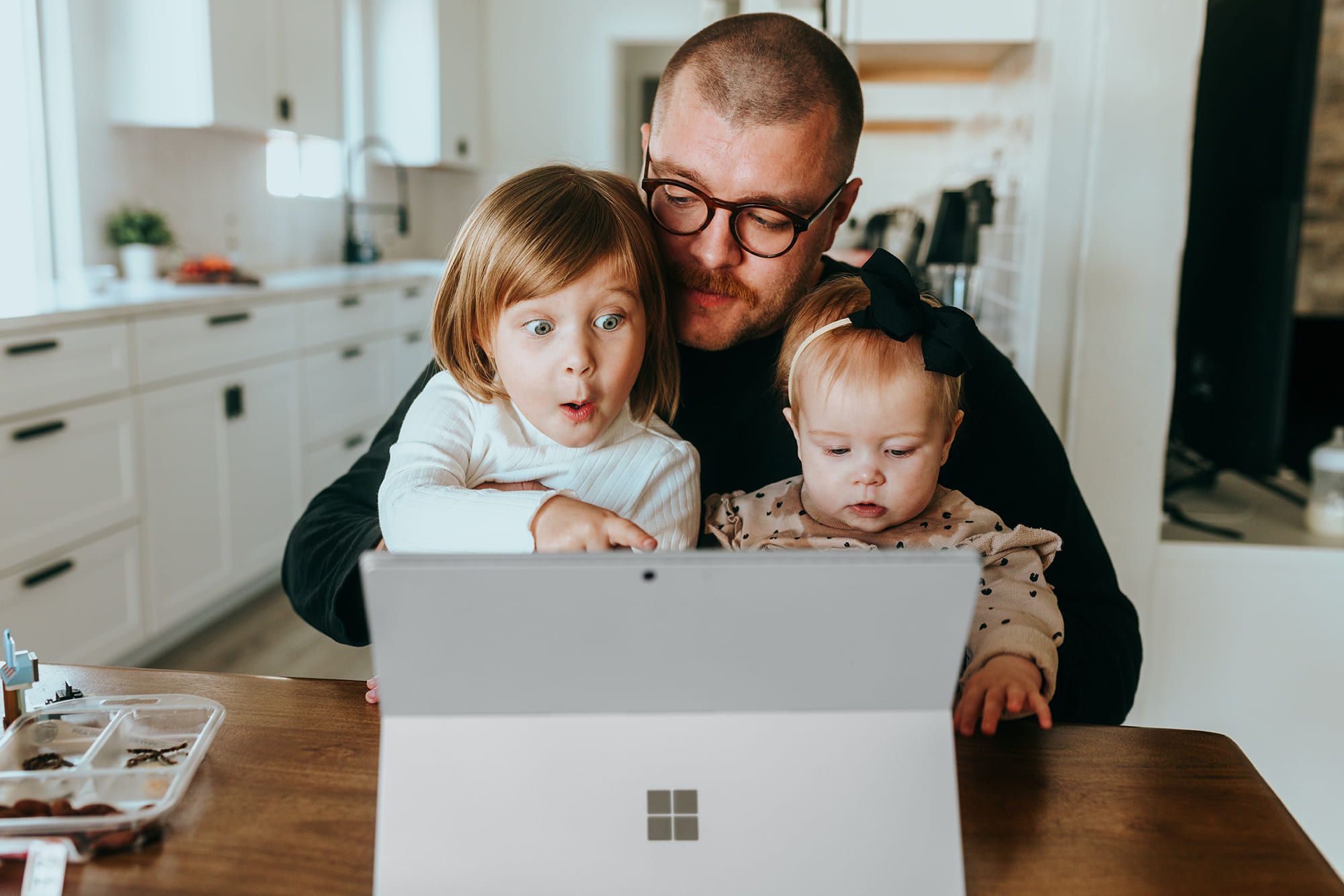 Man holding his young kids in his lap while looking at laptop